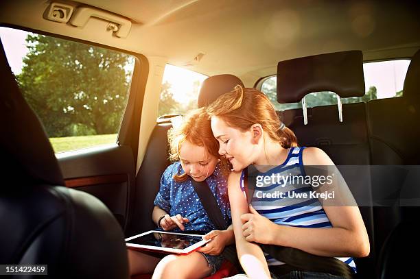 two girls in rear seat of car - girl in car with ipad stock-fotos und bilder