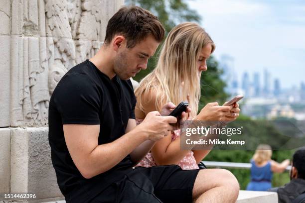 Young adults on their smartphones in Greenwich Park on 8th July 2023 in London, United Kingdom.