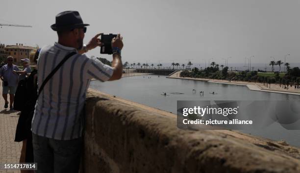 July 2023, Spain, Palma: Tourists take pictures with their cell phones during the heat wave in Mallorca. Rising temperatures of almost 40 degrees are...