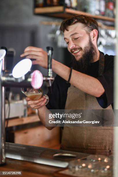 smiling male bartender happy with pouring the beer behind counter - beer tap stockfoto's en -beelden