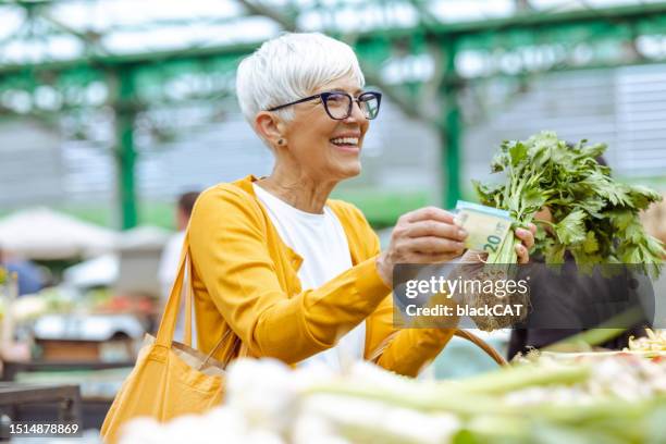 seniorin mit kurzen haaren kauft frisches gemüse und bezahlt mit bargeld - women euro stock-fotos und bilder