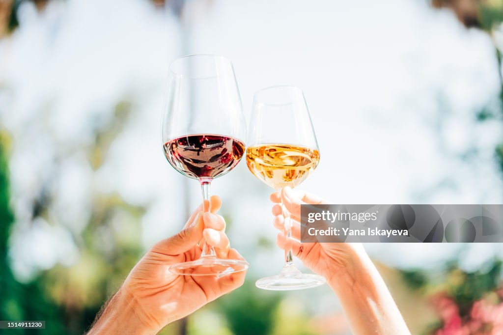 A close-up shot of a couple clinking organic sparkling wine glasses on a sunny day