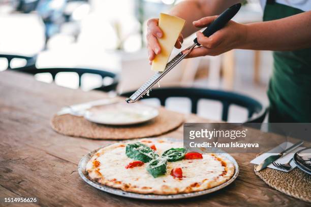 an italian chef generously grating cheddar cheese on a freshly cooked hot oven pizza - pizza napoletana fotografías e imágenes de stock