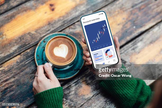 overhead view of young woman checking stock market data on smartphone while drinking coffee - bear and bull stock pictures, royalty-free photos & images
