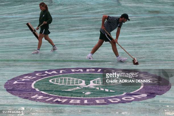 Members of the staff mop a protective cover over the court after the rain started on the sixth day of the 2023 Wimbledon Championships at The All...