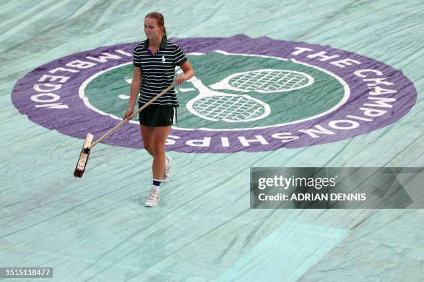 Members of the staff mop a protective cover over the court after the rain started on the sixth day of the 2023 Wimbledon Championships at The All...