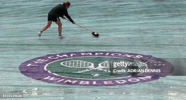 Members of the staff mop a protective cover over the court after the rain started on the sixth day of the 2023 Wimbledon Championships at The All...