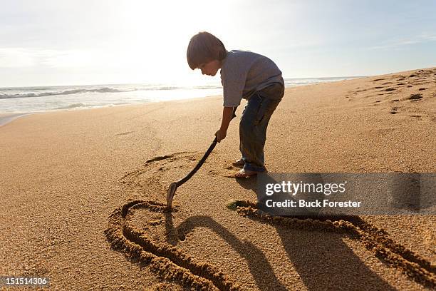 young boy doodles with stick - drawing in sand with stick stock pictures, royalty-free photos & images