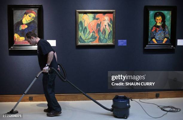 Christie's employee vacuums the carpet in front of paintings on display at Christie's auction house in London, 31 January 2008. The Impressionist and...