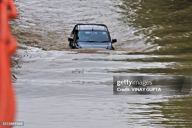 Commuter drives his car through a flooded road after heavy monsoon rains in Gurgaon on the outskirts of New Delhi on July 9, 2023.