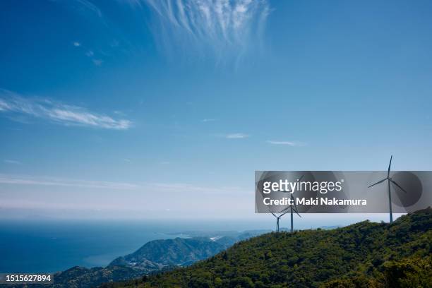 wind turbines spinning across the blue sky and green meadows. - wind power japan stock pictures, royalty-free photos & images