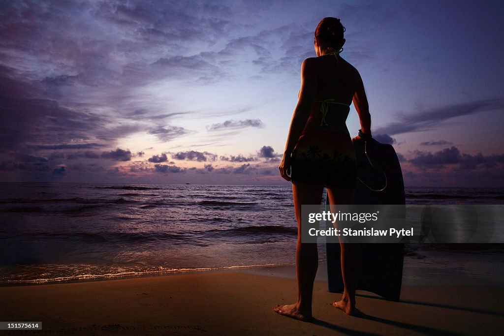 Women with bodyboard looking at sunset on sea