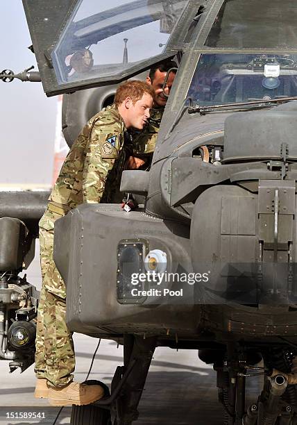 Prince Harry climbs up to examine the cockpit of an Apache helicopter with a member of his squadron on September 7, 2012 at Camp Bastion,...