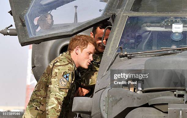 Prince Harry climbs up to examine the cockpit of an Apache helicopter with a member of his squadron on September 7, 2012 at Camp Bastion,...