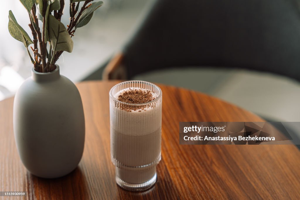 Chocolate milkshake in a glass cup on a wooden table with a vase