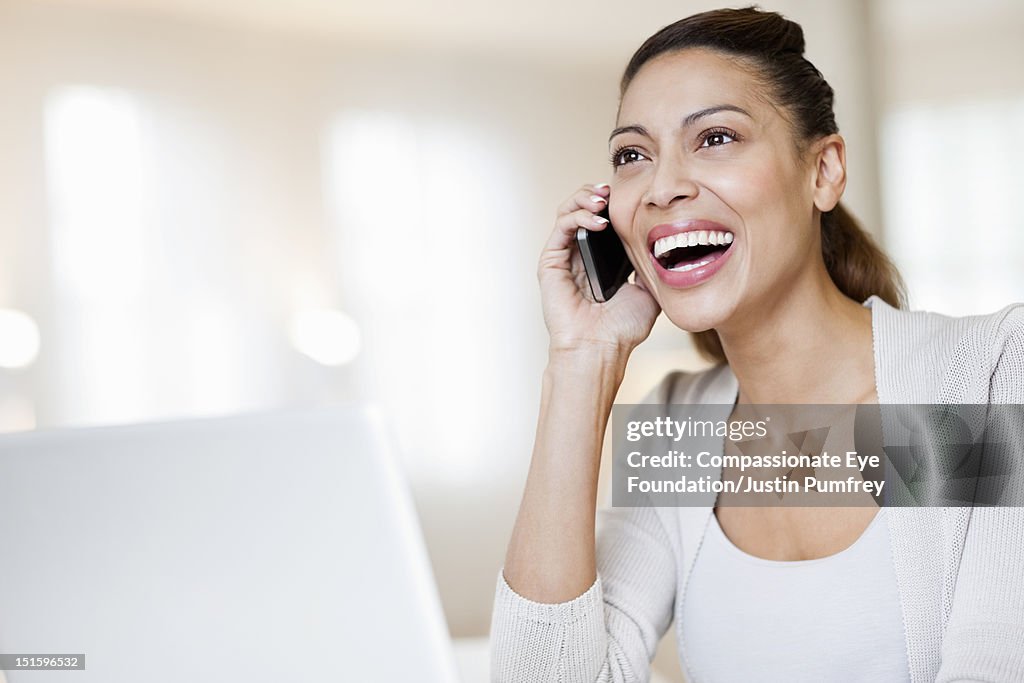 Woman using mobile phone and laptop, smiling