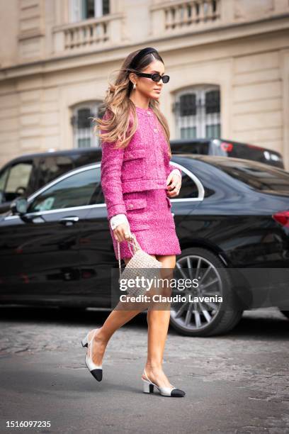 Camila Coelho wears a fuchsia tweed Chanel jacket with matching mini skirt, black headband, silver bag and silver crystals Chanel slingback heels,...