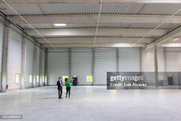 woman with businessman in a new and large empty industrial building - business women looking at new office space stockfoto's en -beelden