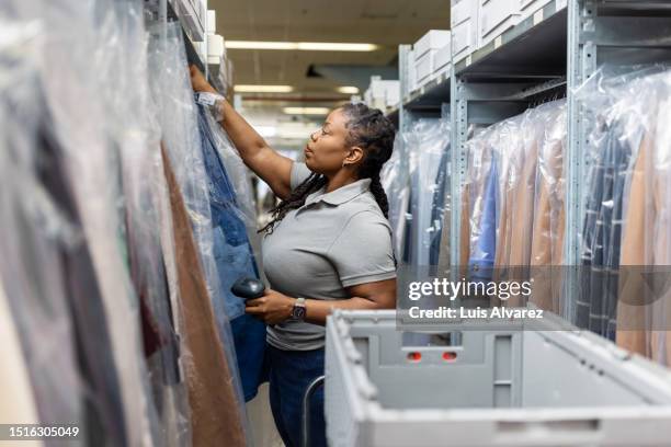 woman employee working in fashion wear section of distribution warehouse - kledinghanger stockfoto's en -beelden
