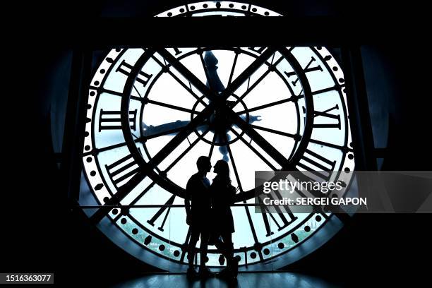 Couple poses for a photo near a giant clock at the Musee d'Orsay in Paris, on July 9, 2023.