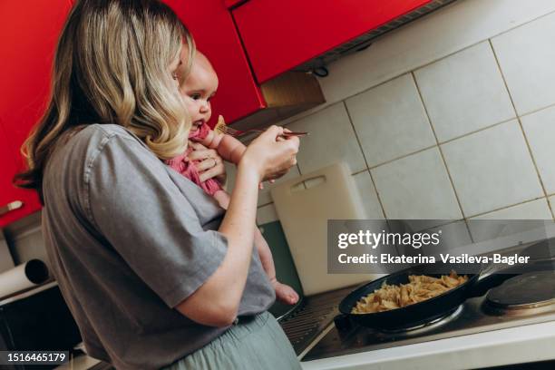 mother with a baby in her arms cooking in the home kitchen concept stay-at-home mother - baby chef stock pictures, royalty-free photos & images