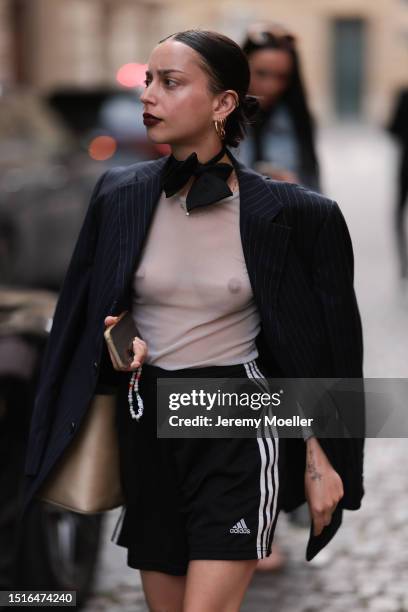 Fashion Week guest is seen wearing golden earrings, a black bowtie, a black oversize pinstriped blazer with grey transparent top underneath, a brown...