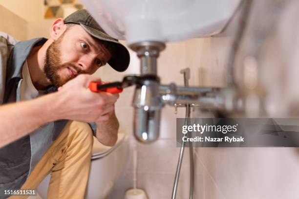 a plumber carefully fixes a leak in a sink using a wrench - plumber stockfoto's en -beelden