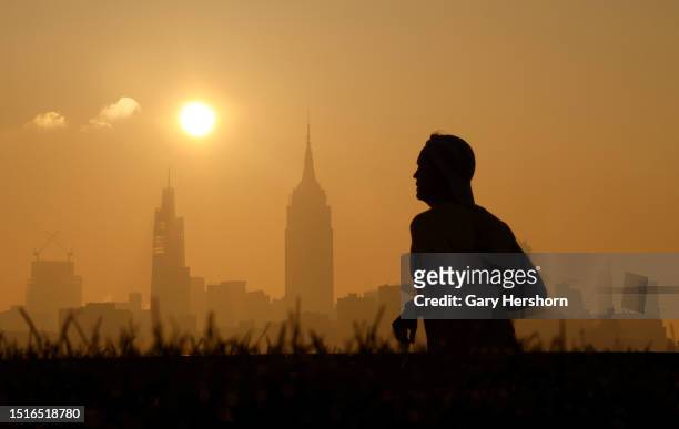 Haze shrouds the skyline of midtown Manhattan and the Empire State Building as the sun rises in New York City as a man runs along the Hudson River on...