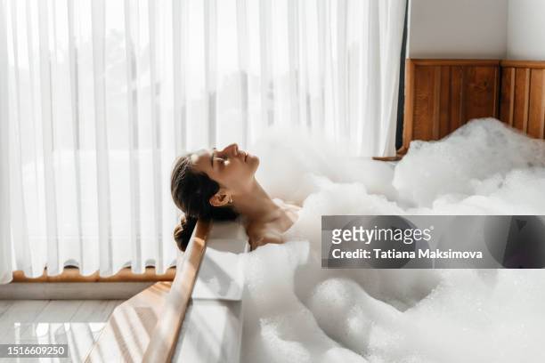 young woman relaxing in bath tub full of foam bubbles. self care and mental health concept. - woman in bathroom stockfoto's en -beelden