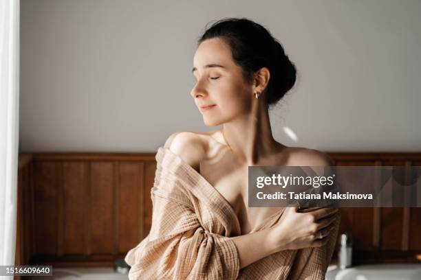 a young beautiful woman in a muslin bathrobe is preparing to take a bath. morning at the hotel, the concept of travel and self-care. - bathrobe stock pictures, royalty-free photos & images