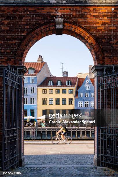 cyclist riding past nyhavn harbour on a sunny summer day, copenhagen, denmark - wonderlust stockfoto's en -beelden