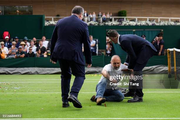 Securities attempt to clear the court after protesters interrupted the Men's Singles first round match between Sho Shimabukuro of Japan and Grigor...