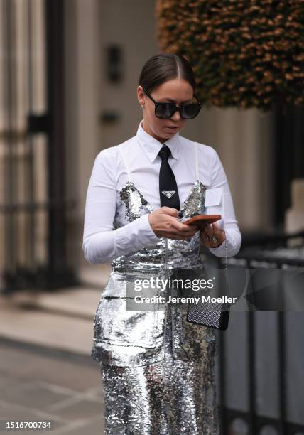 Fashion Week guest is seen wearing big black sunglasses, a shiny silver dress with sequins, underneath a white shirt with collar and a black tie from...