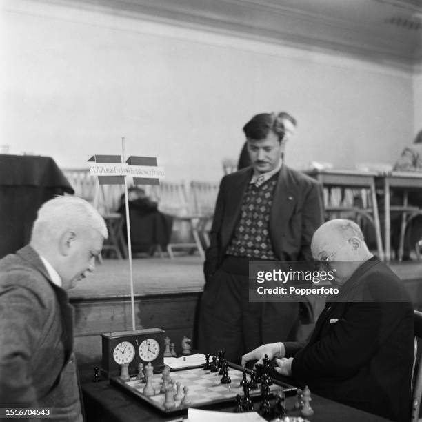 American chess player Herman Steiner stands behind to watch a game between, on left, Sir George Thomas, 7th Baronet of England and, on right, Polish...
