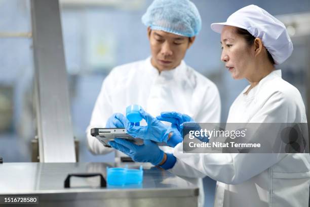 every filled bottle must be checked to ensure it has been sealed securely. a quality control manager and engineer discuss a bottle cap quality for mineral water in a filling process on a conveyor belt in a water bottling plant. - waterzuivering stockfoto's en -beelden