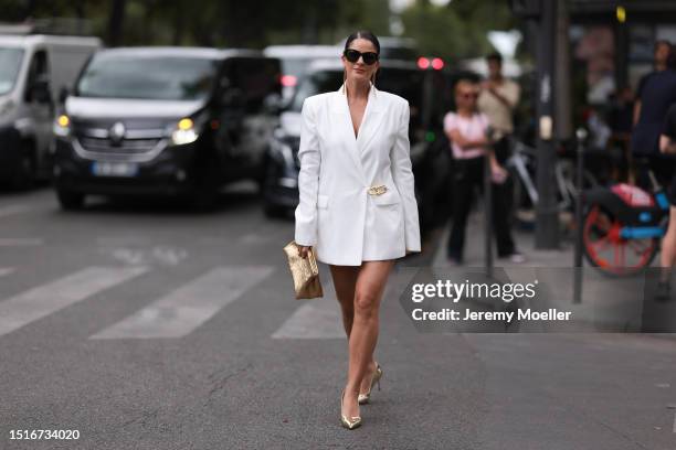 Fashion Week guest is seen wearing big black sunglasses in butterfly shape, long golden chain earrings, a long white buttoned blazer, a shiny...