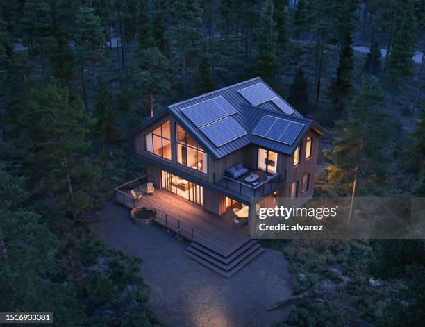 3d render of modern forest house with solar panels on roof at night - illuminated house stock pictures, royalty-free photos & images