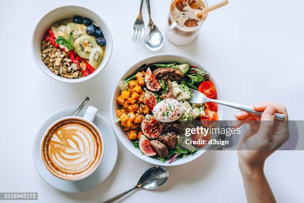 table top view of a woman eating healthy beef cobb salad bowl with greens, avocado, cherry tomatoes, figs, pumpkin and soft boiled egg, vegan chia and quinoa granola fruit bowl and coffee by the side. healthy food trend. nutritious and well-balanced diet - cobb salad overhead stock pictures, royalty-free photos & images