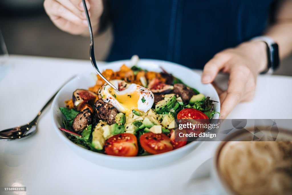 Close up shot of a woman eating a dish of fresh beef cobb salad with a soft boiled egg and coffee at a cafe table. Enjoying her healthy and nutritious lunch. Maintaining a healthy and well-balanced diet. The concept of healthy eating lifestyle
