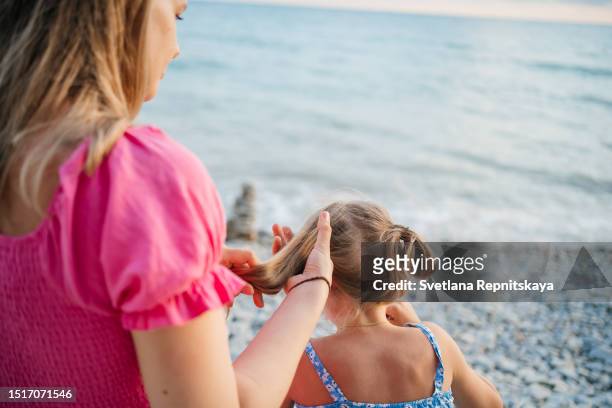 mother doing her daughter's hair on the beach - babysit stockfoto's en -beelden