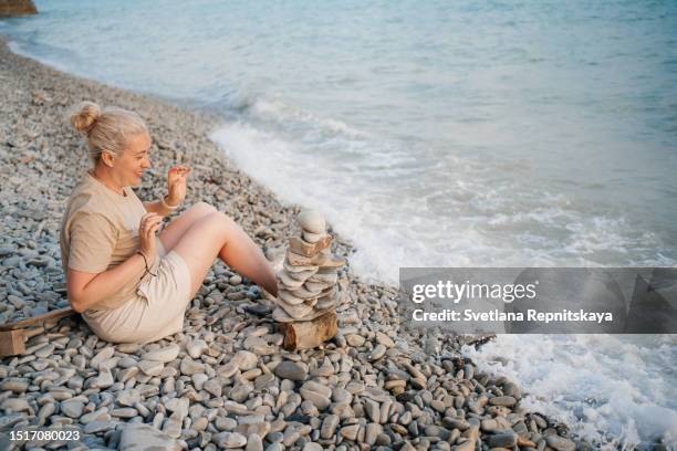 woman building a pyramid of pebbles on the seashore - pyramid rock beach fotografías e imágenes de stock