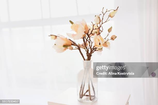 bouquet of sprigs of blooming pink artificial magnolia in clear glass vase - magnolia stellata stockfoto's en -beelden