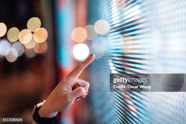 close-up of female finger touching futuristic led display board in the city - hand touch stock pictures, royalty-free photos & images