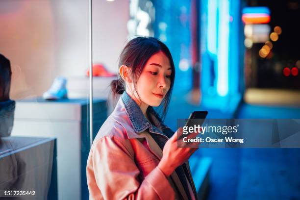 young asian woman using smartphone against retail window display in the city - prospect stock pictures, royalty-free photos & images