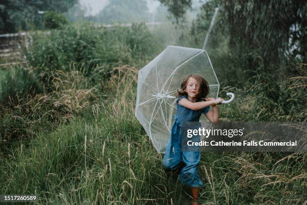 a little girl runs towards the viewer, clutching an umbrella, as heavy rain falls from the sky - see through shoe stock pictures, royalty-free photos & images