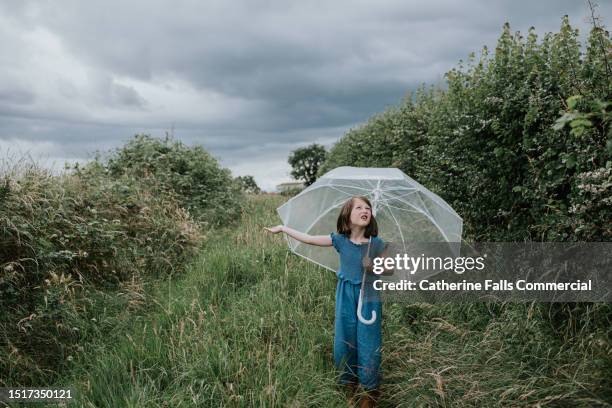 a child under an umbrella puts her hand out, expecting to feel raindrops imminently - girl shower stock pictures, royalty-free photos & images