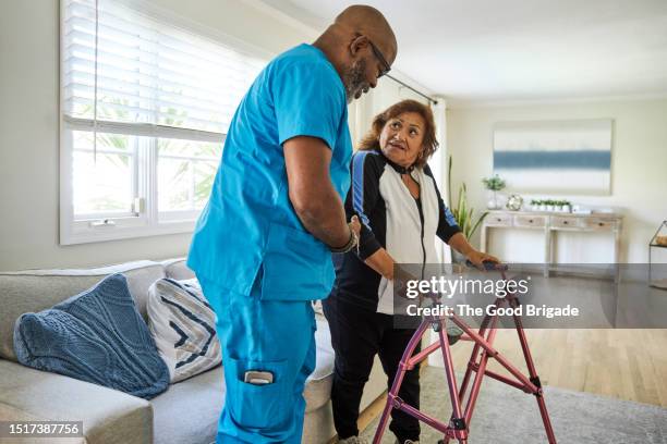 male caregiver assisting senior woman with mobility walker at home - ergotherapie stockfoto's en -beelden