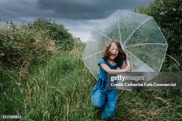 a little girl runs towards the viewer, clutching an umbrella, as rainfall begins - garder photos et images de collection