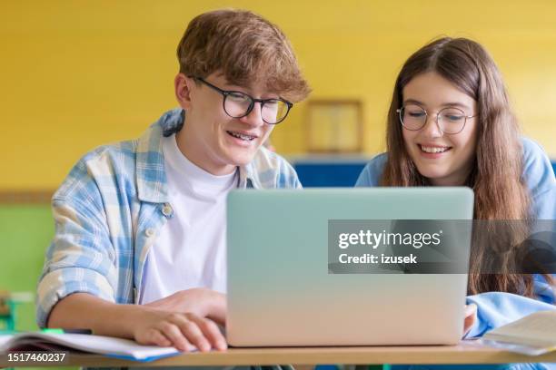 adolescentes sonrientes usando una computadora portátil durante la lección - boy and girl talking fotografías e imágenes de stock