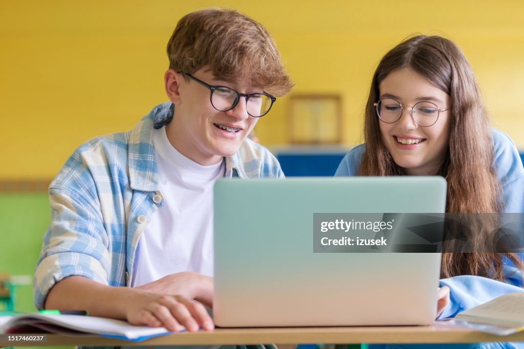 Smiling teenagers using laptop during lesson
